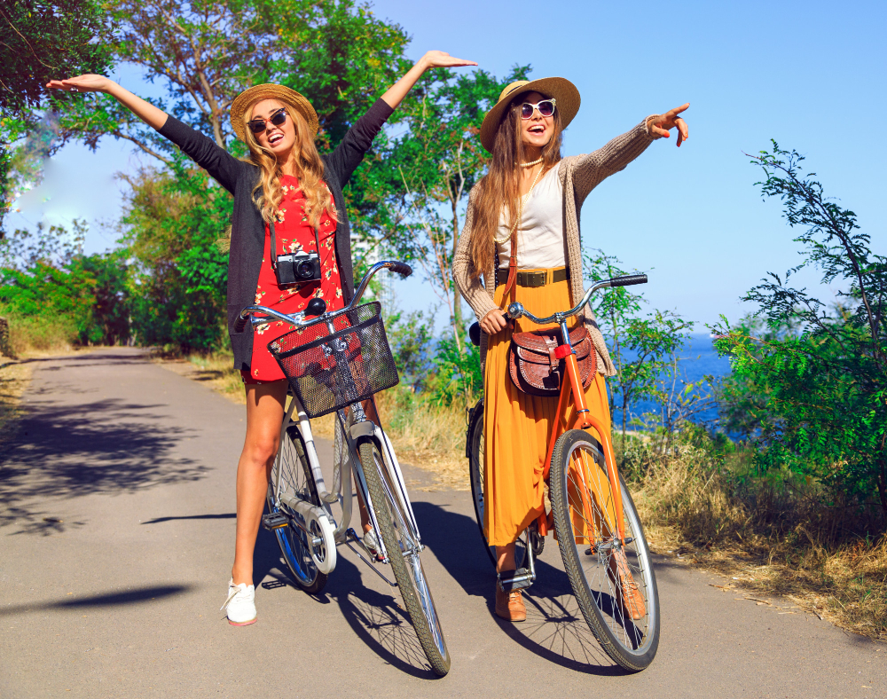 Outdoor sunny fashion portrait of two pretty funny girls, having fun together and going crazy, riding vintage hipster bikes, waring vintage clothes hats and sunglasses. positive mood.